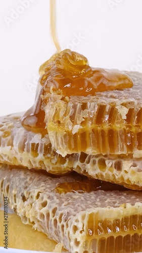 Vertical shot of Fresh honey pouring over stacked honeycomb pieces, close-up shot on white background