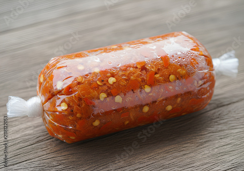 Spicy red chili paste in plastic wrap on wooden background