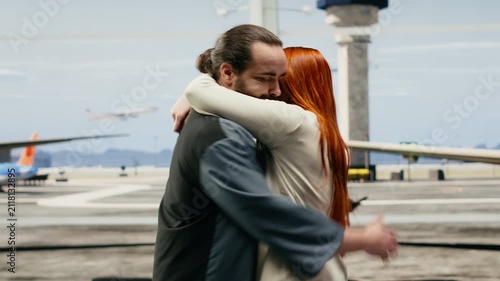 A boyfriend and girlfriend reunite in an airport terminal, hugging and smiling with joy after arrival during an affectionate homecoming.