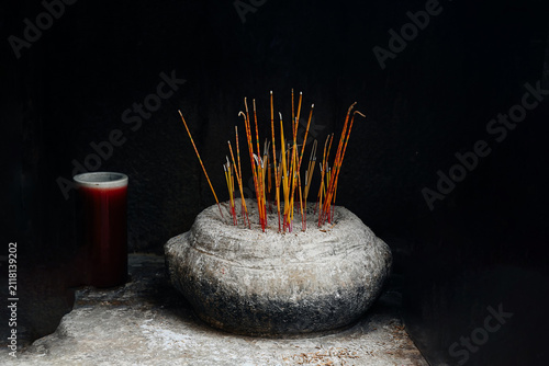Burning traditional joss incense sticks in a rustic stone burner against dark black background inside chinese temple