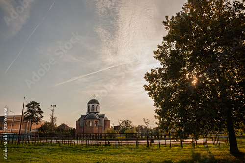 Foto Hram Svetog Ilije, the Saint Elijah Serbian Orthodox church in Jabuka, Vojvodina, Serbia, seen at dusk beside deserted streets in the quiet rural landscape of the Banat region with warm evening light