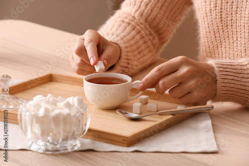 Картината върху платно Woman adding sugar cube to a cup of hot tea on a wooden tray, sweetening beverag