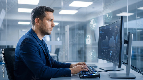 Businessman monitors secure network traffic and digital assets on a curved desktop computer screen while working in a modern office environment during a late shift.