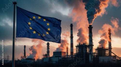 European Union flag waves before industrial complex at sunset. Smoke billows from factory chimneys into cloudy sky. Heavy manufacturing plant emits gases. Air pollution climate crisis impact on