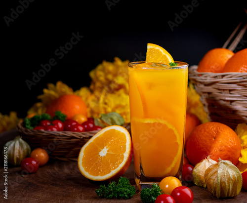 Glass of organic orange juice surrounded by fresh fruits and vegetables on dark wooden background, healthy drink concept