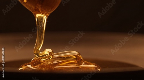 golden honey flowing in thick ribbon on a dark background for culinary use