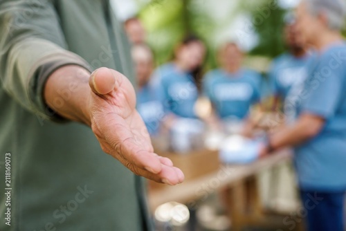 leadership development nonprofits volunteer concept. Outstretched hand of a person offering help with volunteers in the background.