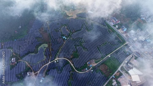 Cinematic aerial: Drone view of solar power installation wrapped in morning fog among green fields and scattered hamlets