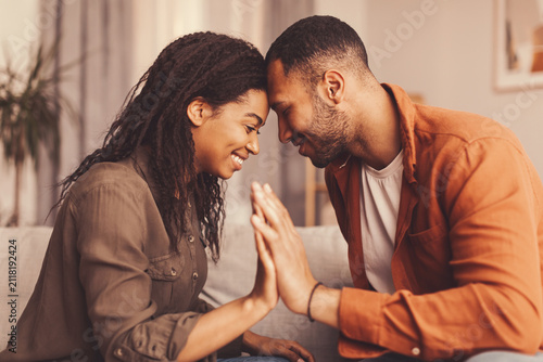 Fotografie Happy African American Couple Engaging In Interaction While Sitting On Couch At Home, Smiling, And Showing Affection