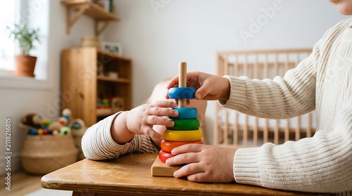 Toddler hands playing with colorful wooden stacking rings toy on table in nursery room for fine motor skills development