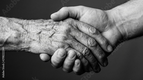 Fotografía Black and white close up of an elderly hand holding a young person hand symboliz
