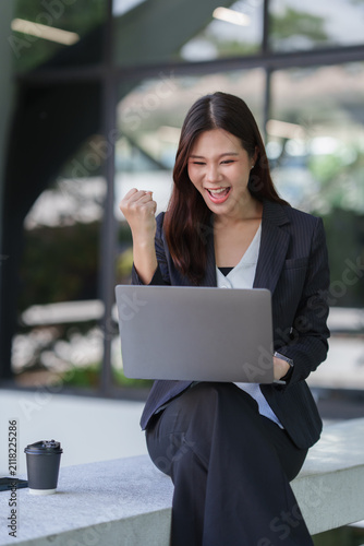 Asian businesswoman celebrating success working on laptop outdoor