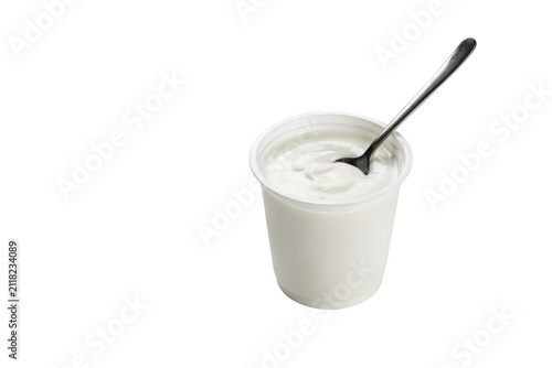 A single white plastic cup filled with creamy plain yogurt and a silver metal spoon resting inside, isolated on a solid black background