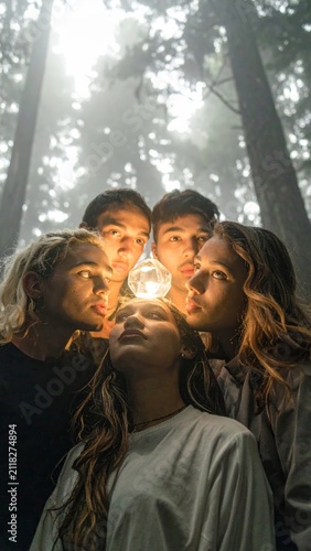 Group of Curious Young People Discovering a Mysterious Glowing Light in a Misty Enchanted Forest