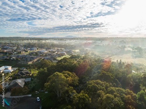 misty sunlit edge of town with houses backing onto trees