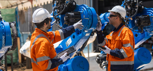 Industrial engineers inspecting robotic automation system in smart factory, using tablets for maintenance, diagnostics and quality control. Advanced manufacturing, Industry 4.0 and workplace safety.