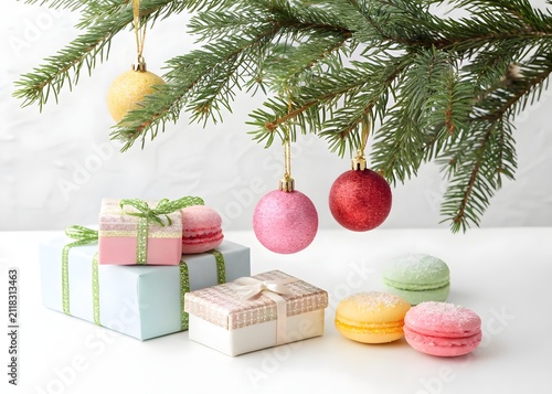 Christmas tree branches with ornaments above pastel gift boxes and macarons on a white surface