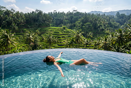Young Balinese woman relaxing in an infinity pool overlooking the lush jungle and terraced rice fields. Luxury wellness travel and tropical escape concept