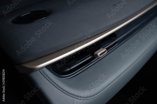 Close‑up of car interior detail highlighting dashboard air vent with metallic adjustment knob. Textured surface contrasts with smooth leather upholstery and visible stitching.