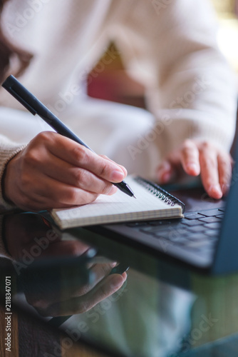 Vertical closeup image of a woman writing on a notebook while working on laptop computer