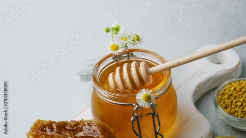 Honey in a glass jar with a wooden dipper and honeycomb on a white board