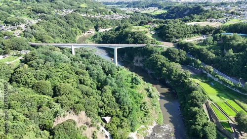 Aerial view of a river flowing through lush green hills. Modern bridge spans the river, connecting both sides. Villages dot the landscape, nestled among trees. Natural beauty surrounds the quiet