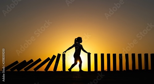 Woman silhouetted with falling dominoes at sunset concept of risk and control