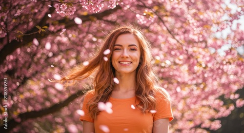 Woman smiling beneath blossoming pink cherry tree with falling petals