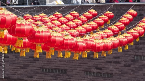 Rows of vibrant red Chinese lanterns hanging against an ancient brick wall background.