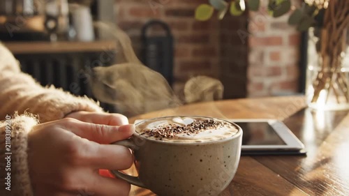 Hands holding steaming coffee cup with tablet on wooden table