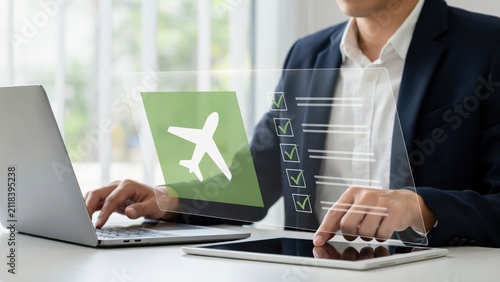 Businessman using laptop and tablet for flight booking with holographic checklist interface