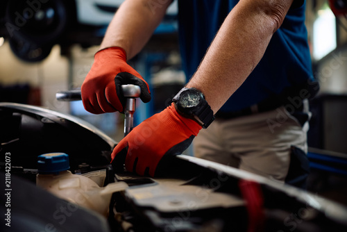 Close up of mechanic using wrench while repairing car engine in a garage.