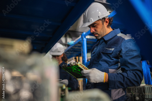 Chief mechanical engineer inspecting examining circuit board motherboard spare parts stock room factory. Concept of industrial maintenance service inspecting management and managing industrial waste.