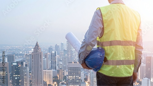 Civil engineer holding helmet overlooking city skyline.