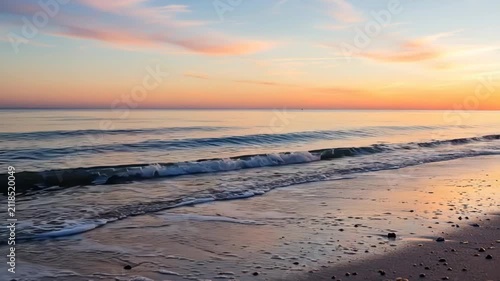 A tranquil ocean shoreline glowing under a soft pastel colored sunrise sky
