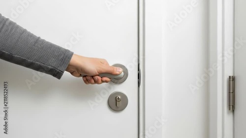 A hand grasping a modern silver door handle on a clean white interior door