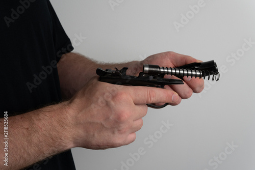 Foto Close up of man hands disassembling semi automatic pistol by separating slide from frame with recoil spring on neutral background