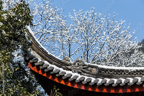 Snowy traditional Chinese temple roof in Hangzhou under winter trees