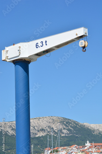 A low angle view captures a blue and white harbor jib crane with a lifting capacity of six point three tons against a clear sky
