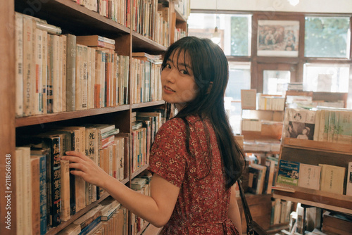 Naklejka 古書店の棚へ手を伸ばす赤い花柄ワンピースの女性