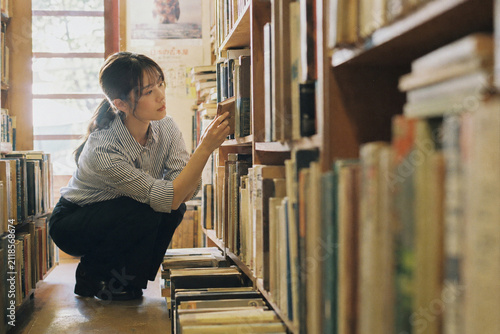 Plakat 古書店の低い棚をしゃがんで探す女性