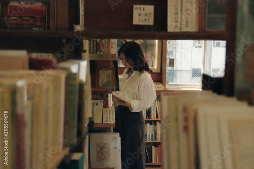 Plakat 古書店の棚で本を探す白いブラウスの女性
