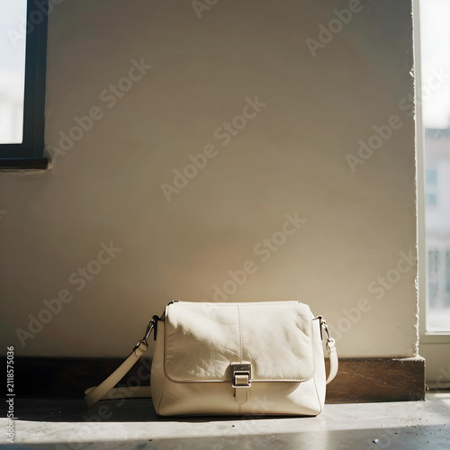 A trendy cream leather crossbody bag sits on a beige wall, perfectly capturing the warmth of north-facing natural light.