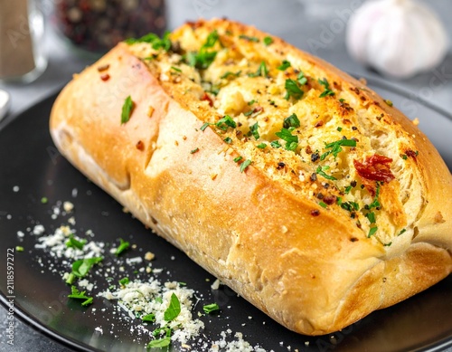 Delicious freshly baked stuffed garlic bread loaded with melted cheese, herbs, and spices on a black plate