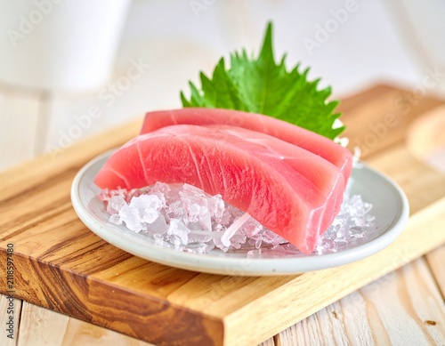 Fresh raw tuna sashimi slices served on crushed ice with shiso leaf on a wooden board for traditional Japanese gourmet dining concept