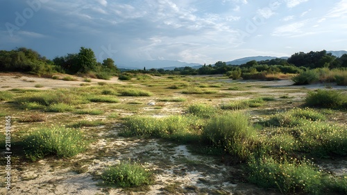 Dry valley scenery featuring sandy river plains, scattered vegetation, distant mountains, and cloudy skies, 