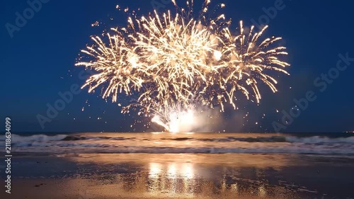 Bright colorful fireworks exploding in the night sky above a dark ocean beach at summer