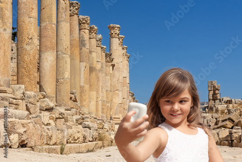 Little tanned girl takes a selfie in the streets of Jerash, lined with the colonnade of the Cardo. Jordan. Horizontally. 