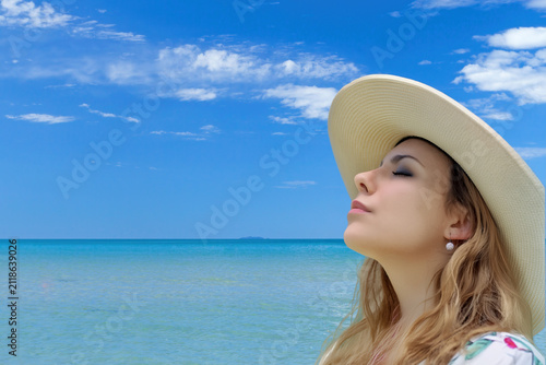 Closeup view of a young woman in a straw hat relaxing on the seashore under a blue sky.The photo has plenty of place for your text.