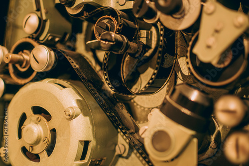 Close-up of a vintage movie projector mechanism showing film strip running through sprockets and gears.